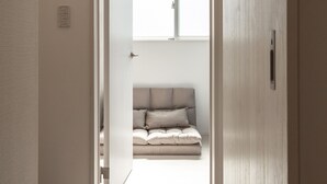 A narrow hallway leading to a bedroom with a bed, a window, and a door. - Private Hotel Oshiage (Tokyo)
