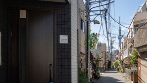 A narrow urban street with a dark brown building entrance, tiled steps, and a visible handrail. - Private Hotel Oshiage (Tokyo)