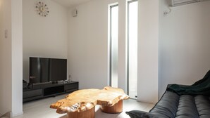 A modern living room with a wooden coffee table, a black leather sofa, and a flat-screen TV on a black stand. - Private Hotel Oshiage (Tokyo)