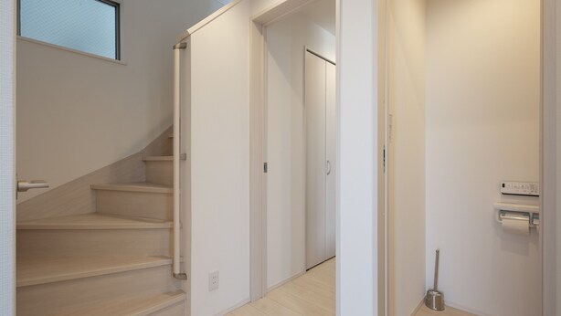 A clean, modern interior with a staircase leading to a door, a small bathroom with a toilet paper holder, and a window providing natural light. - Private Hotel Oshiage (Tokyo)