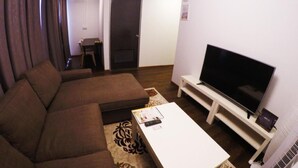 Een woonkamer met een bank, een bijzettafeltje, een televisie op een meubel en een deur op de achtergrond.