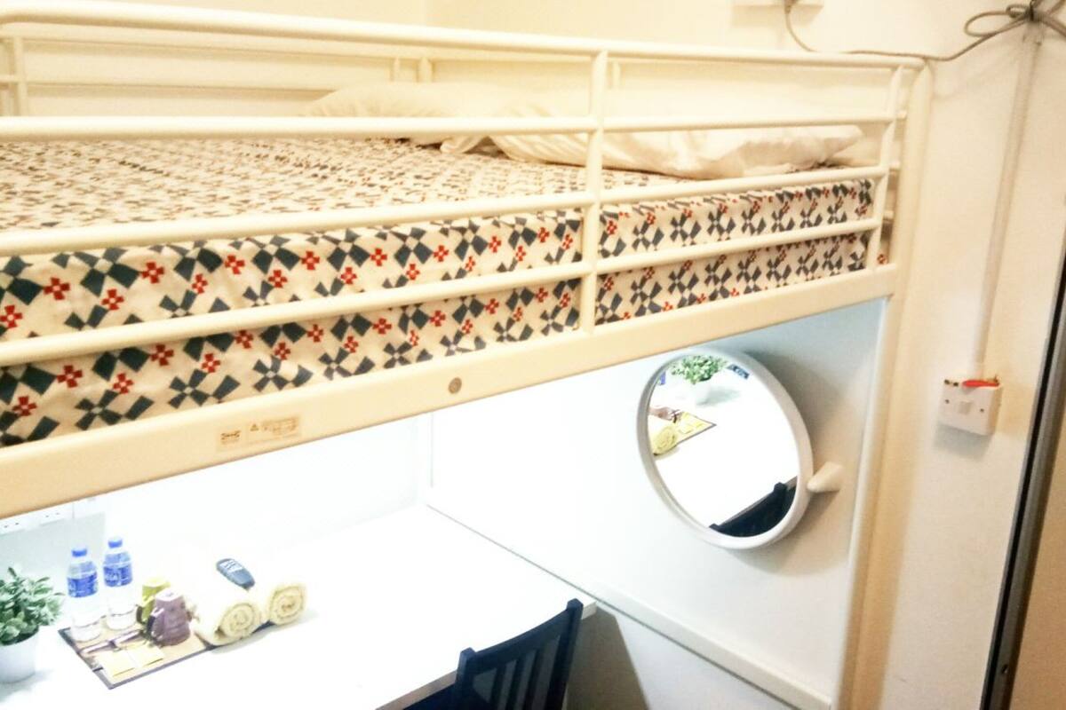 Ein Etagenbett mit gemusterten Betttextilien, ein runder Spiegel, ein kleiner Schreibtisch mit Pflanze und ein Stuhl.