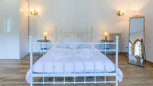 A neatly arranged bedroom with a white metal bed frame, two bedside tables with lamps, a large mirror, and a radiator. - Beautiful apartment in villa for 10 guests with private pool, WIFI, TV, terrace and pets allowed (Greve In Chianti)
