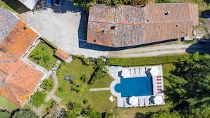 Luchtbeeld van een bezit met een zwembad, omringd door een terras, een tennisbaan en een overdekt gedeelte met zitplaatsen.