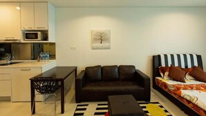 A compact living space with a kitchenette, a black leather sofa, a striped bed, and a painting of a tree on the wall. - Resort Hostel In City (Kuala Lumpur)
