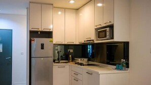 A compact kitchen with white cabinets, a stainless steel refrigerator, a microwave, and a gas stove. - Resort Hostel In City (Kuala Lumpur)