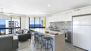 A modern kitchen with a large island, bar stools, and a view of the city. - Victoria Square Private Apartments (Broadbeach)
