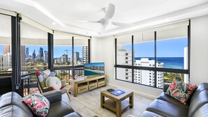 A modern living room with a city view, a ceiling fan, and a pool table. - Victoria Square Private Apartments (Broadbeach)