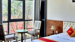 A hotel room with a bed, a small table, two chairs, and a view of the city through large windows. - S79 Anh Duc Hotel 2 (Ho Chi Minh City)
