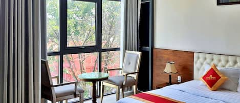 A hotel room with a bed, a small table, two chairs, and a view of the city through large windows.