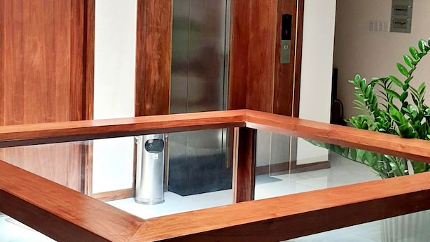 A modern elevator with a wooden frame and glass doors, a wooden bench in the lobby, and a potted plant. - S79 Anh Duc Hotel 2 (Ho Chi Minh City)