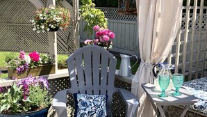 Een terras met een witte stoel, een tafeltje met twee glazen en een hangende bloempot.