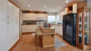 Een moderne keuken met witte kastjes, een houten eiland, een zwarte koelkast en uitzicht op de omgeving door grote ramen.