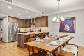 A modern kitchen with wooden cabinets, a stainless steel refrigerator, and a dining area with a wooden table set for six.