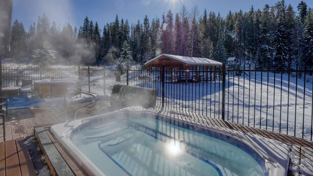 Ein Whirlpoolbereich mit Holzterrasse, umgeben von einem Metallzaun, und eine kleine Holzhütte in einem verschneiten Wald.