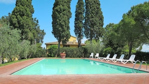 A swimming pool with lounge chairs, surrounded by tall trees and a building in the background. - Nice apartment for 4 people with WIFI, pool, TV, patio, pets allowed and panoramic view (Tavarnelle Val Di Pesa)