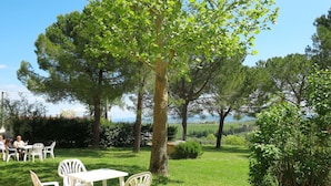An outdoor seating area with white plastic chairs and tables, surrounded by lush greenery and trees. - Nice apartment for 4 people with WIFI, pool, TV, patio, pets allowed and panoramic view (Tavarnelle Val Di Pesa)
