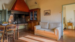 A cozy living room with a fireplace, a dining area with chairs, a sofa, and a cabinet with glass doors. - Nice apartment for 4 people with WIFI, pool, TV, patio, pets allowed and panoramic view (Tavarnelle Val Di Pesa)