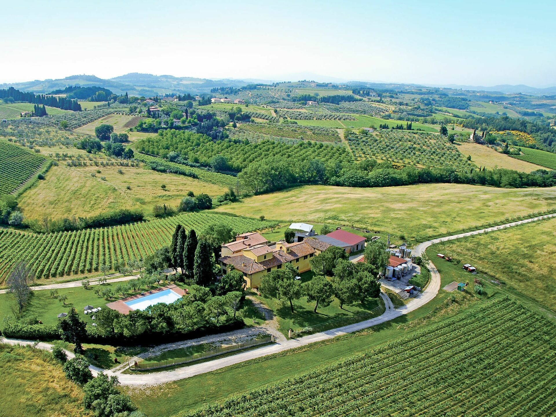 An aerial view of a vineyard with terraced fields, a central building with a red roof, and a swimming pool.