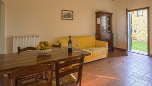 Zona pranzo con tavolo apparecchiato per due, una ciotola di frutta e una bottiglia di vino. Sullo sfondo, un divano giallo e un mobiletto in legno.
