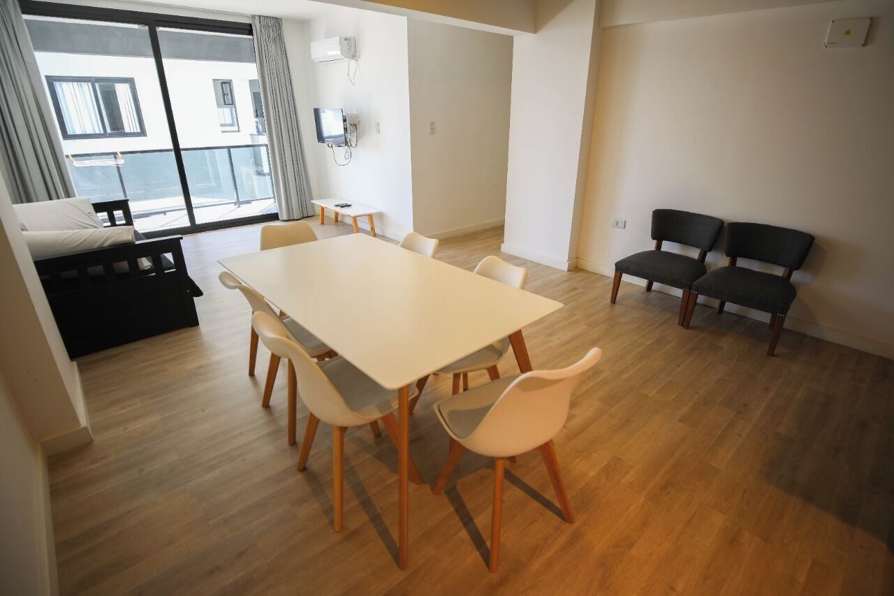 Ett modernt vardagsrum med ett stort vitt bord och stolar, en soffa och en balkong med utsikt.