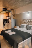 Una habitación de hotel moderna con una colcha negra, un cabecero acolchado y una escalera de metal negra con un letrero que dice 'ANDREW'.