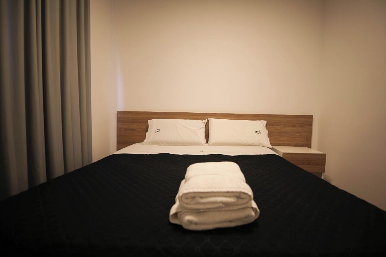 A neatly made bed with a black bedspread and two pillows, a folded towel on the bed, and a wooden headboard.