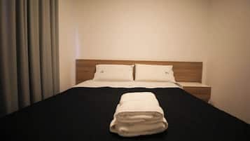 A neatly made bed with a black bedspread and two pillows, a folded towel on the bed, and a wooden headboard.