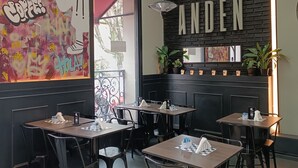 A restaurant interior with tables, chairs, a mural, a sign reading "ANDÉN", and a black brick wall. - Anden by FMA Coliving (Salta)