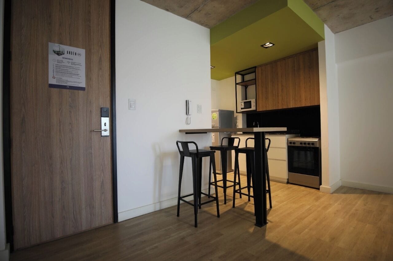 Une cuisine moderne avec des meubles en bois, un four à micro-ondes et une cuisinière. On y trouve trois tabourets de bar noirs et un comptoir blanc.