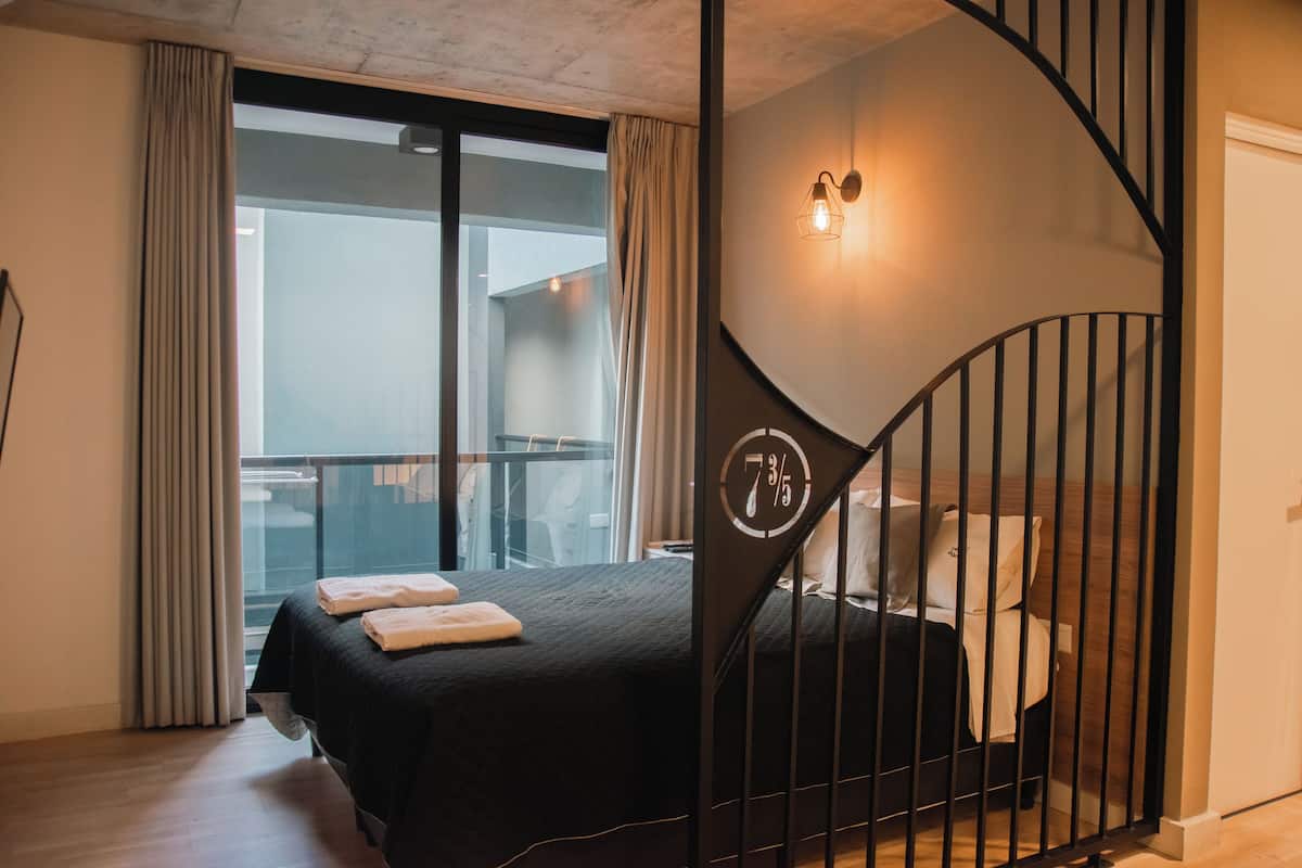 A modern hotel room with a large bed, a balcony, and a staircase with a unique design.