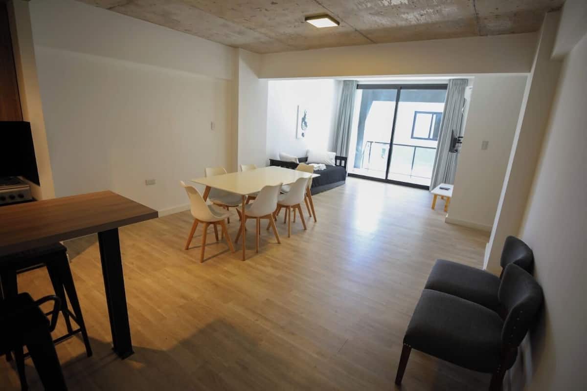 A spacious living area with a wooden floor, a dining table with chairs, a sofa, and a black armchair.