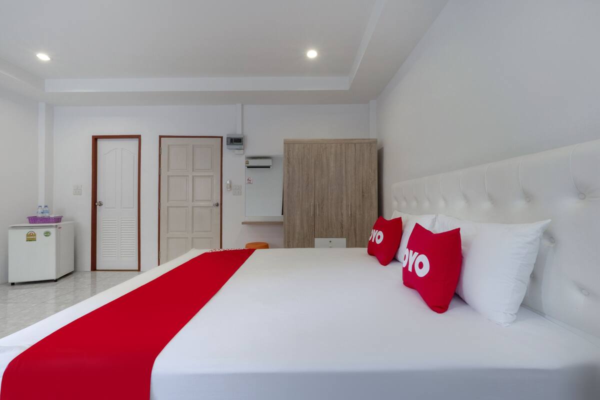 Ein Hotelzimmer mit einem großen Bett, einem Schrank, einer kleinen Kühlbox und einer Tür.