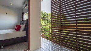 Un balcon donnant sur un espace verdoyant, un lit avec une tête de lit et une fenêtre avec des rideaux.