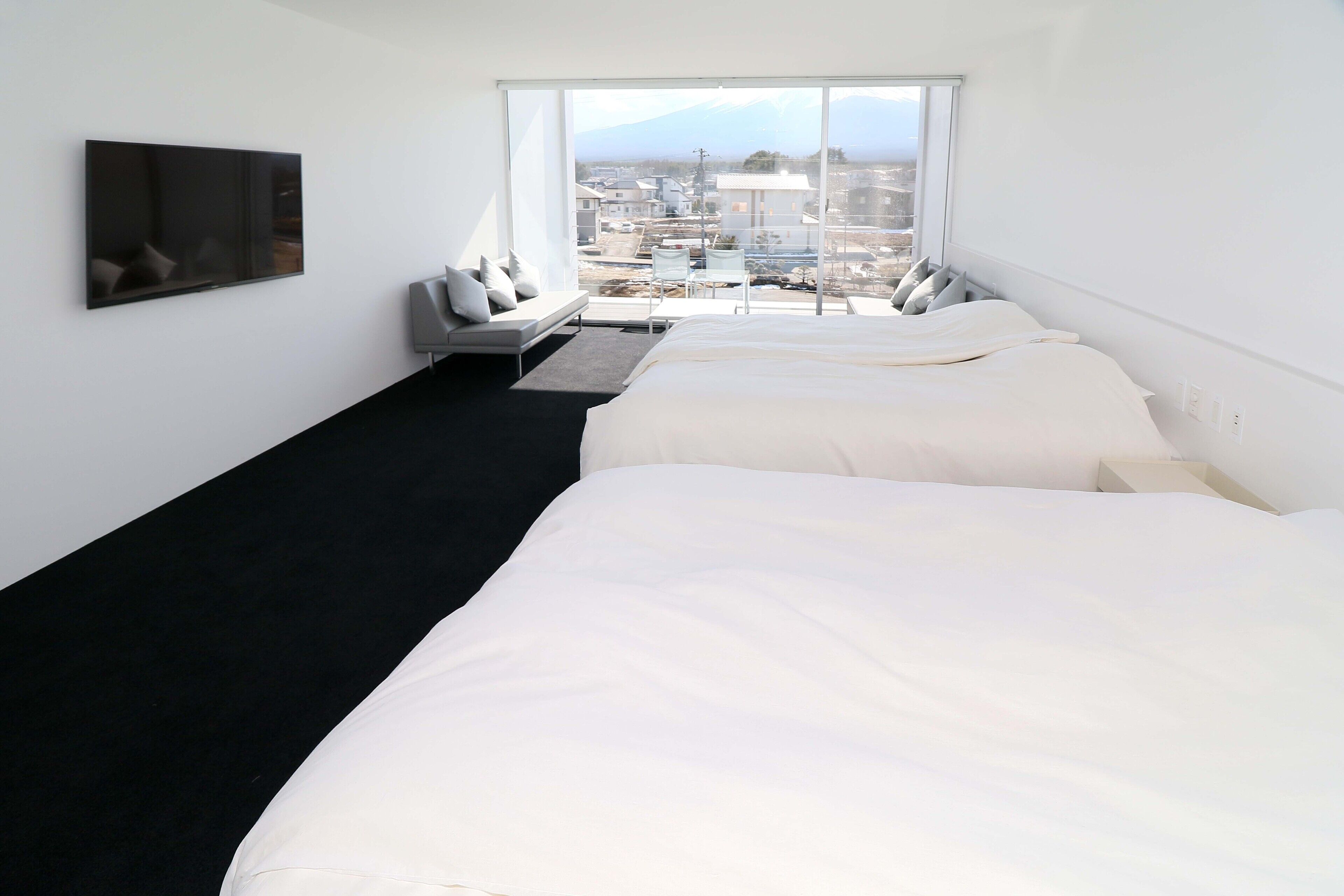 Een hotelkamer met twee bedden, een televisie, een bureau en een groot raam met uitzicht op de stad.