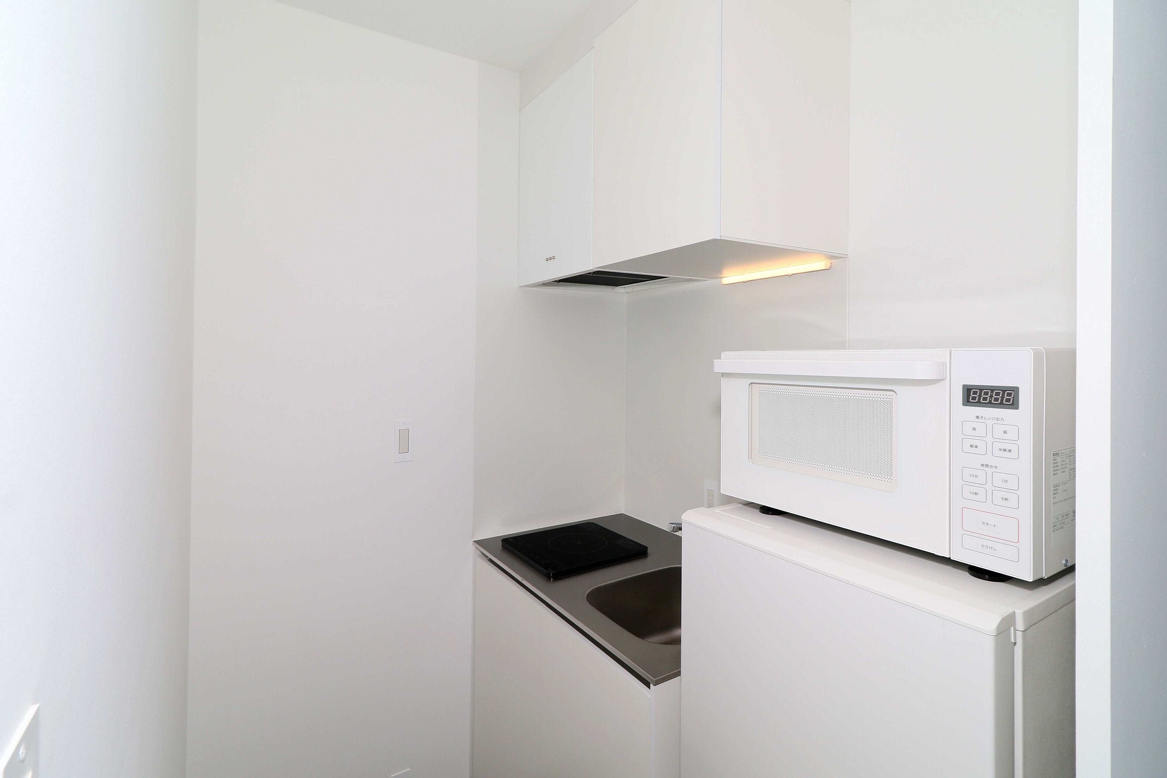 Uma cozinha compacta com micro-ondas integrado e fogão por indução de aço inoxidável.