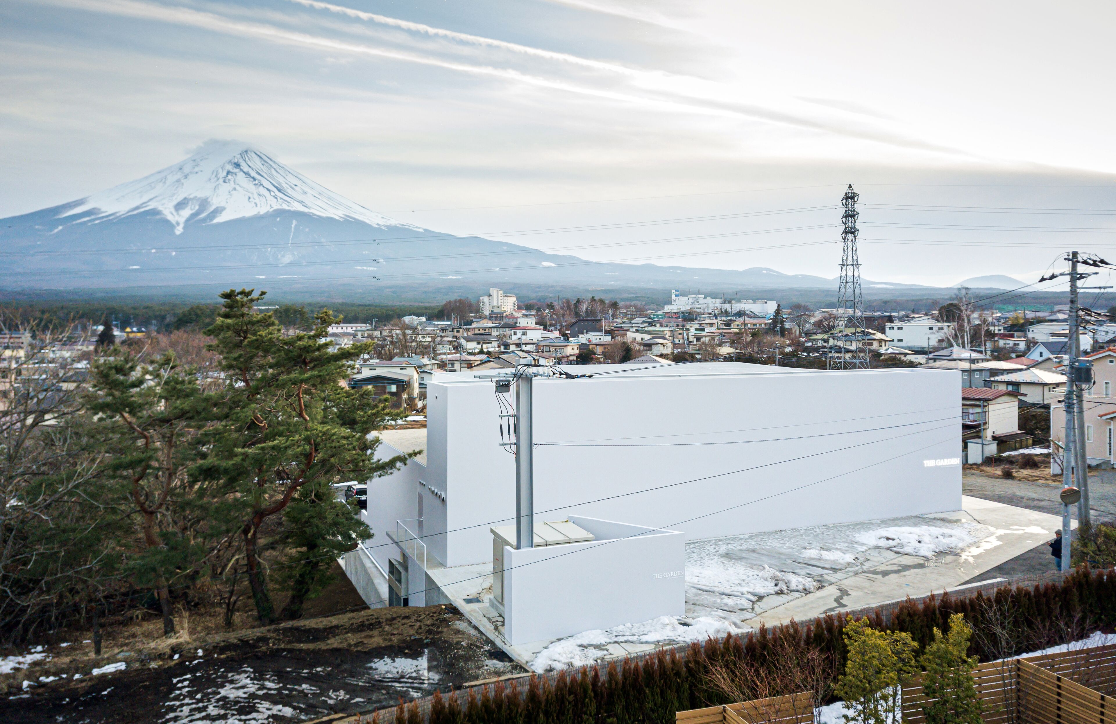 A modern building with a flat roof and a large white wall, located near a snowy landscape with a mountain in the background.