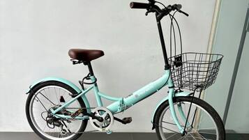 A teal bicycle with a brown seat, a front basket, and a rear rack, parked against a wall.