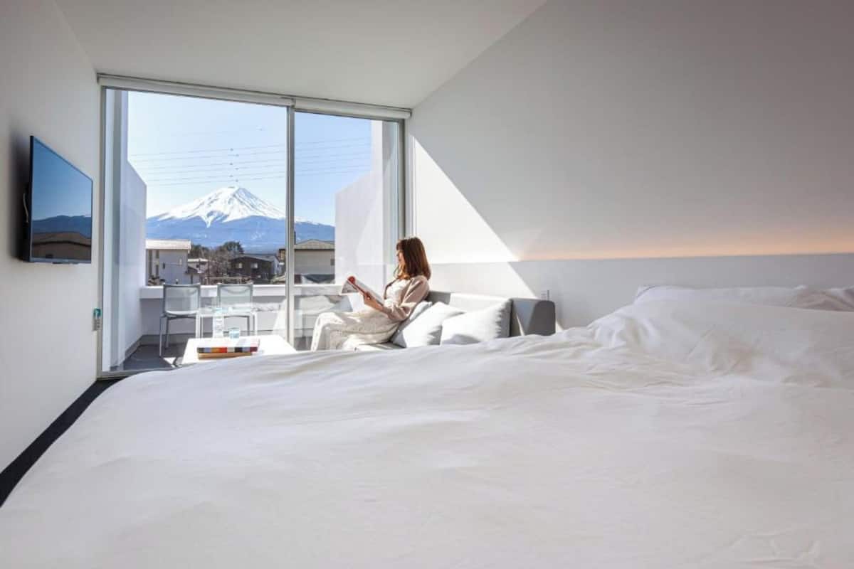 A hotel room with a bed, a desk, and a large window with a view of a mountain.