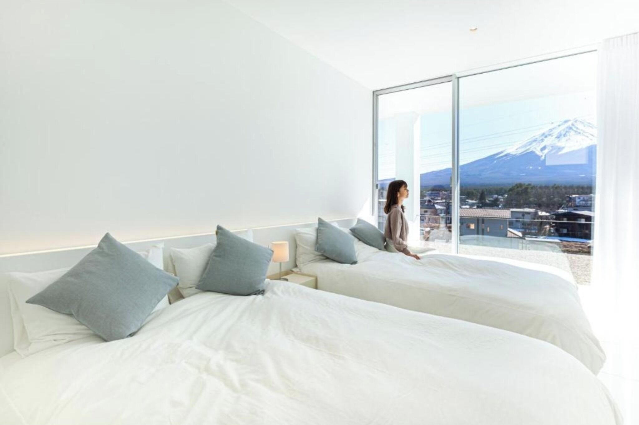 Une chambre d’hôtel moderne avec deux lits, une grande fenêtre donnant sur les montagnes et une table de chevet avec une lampe.