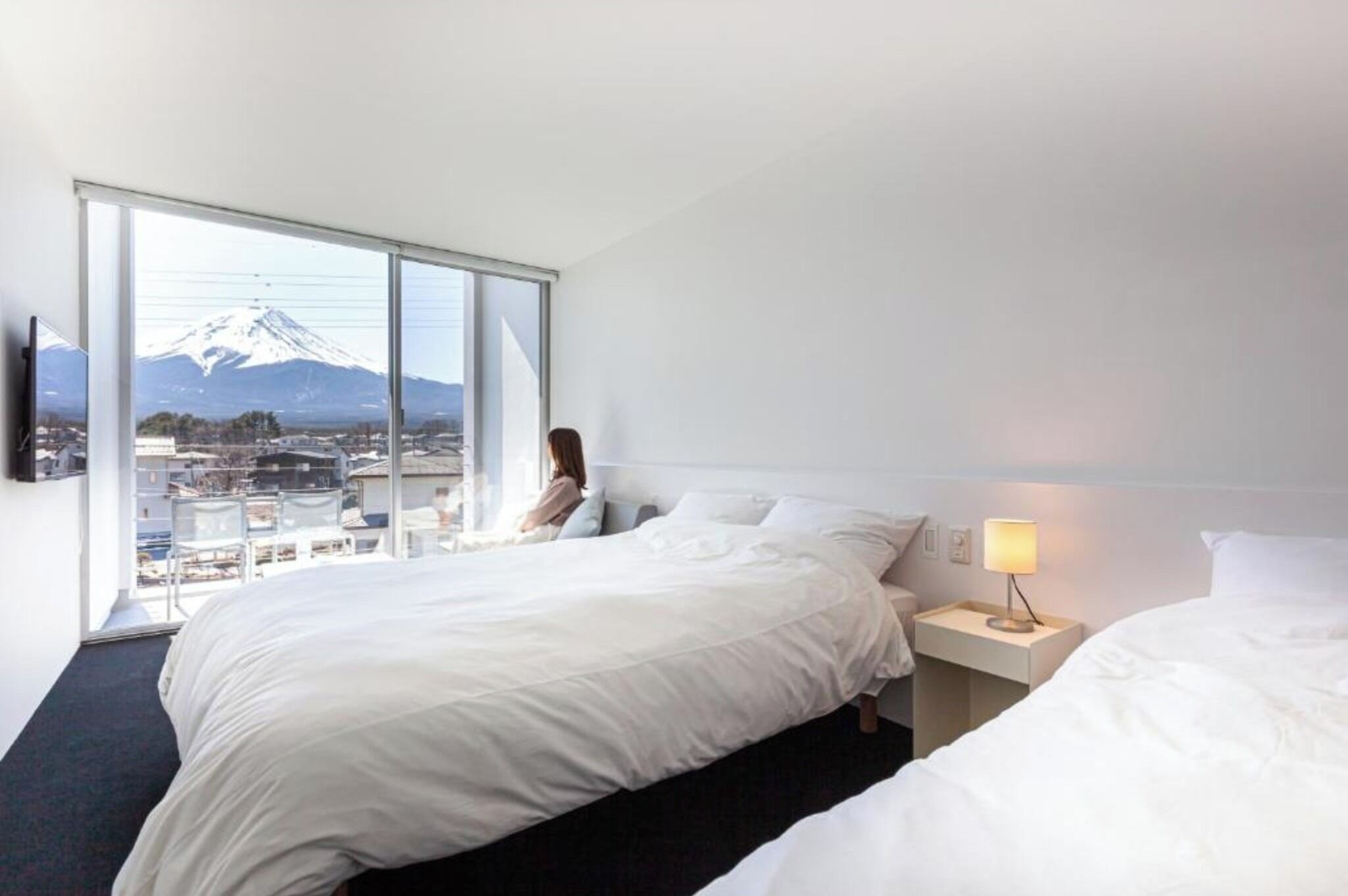 Une chambre d’hôtel avec une grande fenêtre, un lit, une table de chevet avec une lampe et une vue sur une montagne.