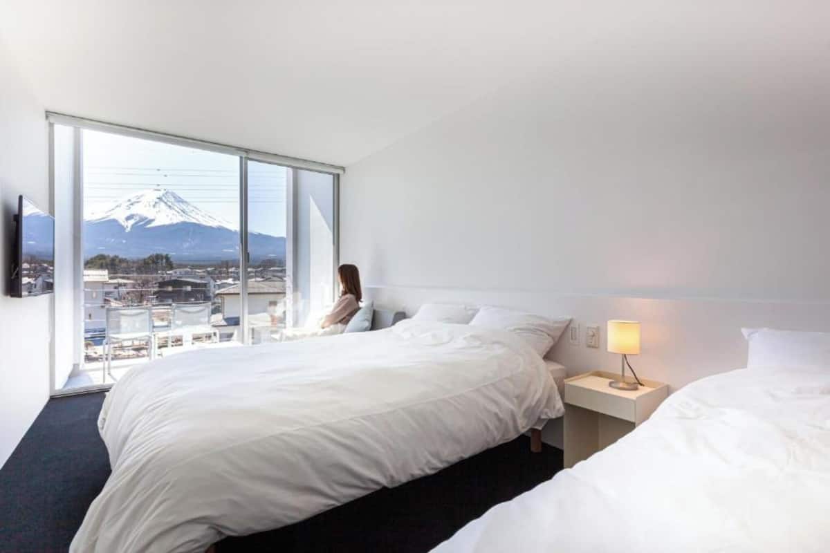 A hotel room with a large window, a bed, a bedside table with a lamp, and a view of a mountain.