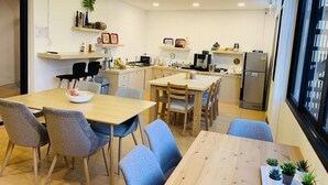 A modern kitchen with a dining area, wooden furniture, and a view of the city through large windows. - Daraya Hostel (Bangkok)