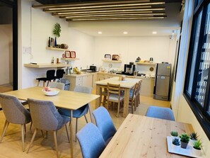 A modern kitchen with a dining area, wooden furniture, and a view of the city through large windows. - Daraya Hostel (Bangkok)