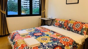 A hotel room with a bed, a small table, a chair, a window with curtains, and a framed picture on the wall. - Daraya Hostel (Bangkok)