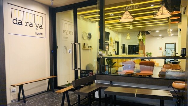 A modern hostel interior with a reception desk, seating area, and a visible sign reading "da ra ya hostel". - Daraya Hostel (Bangkok)