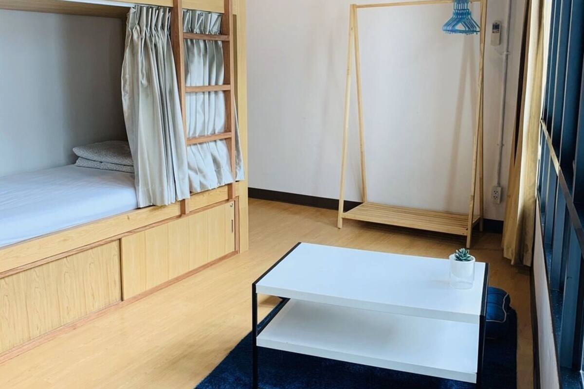 A dorm-style room with bunk beds, a small table, and a hanging light fixture.