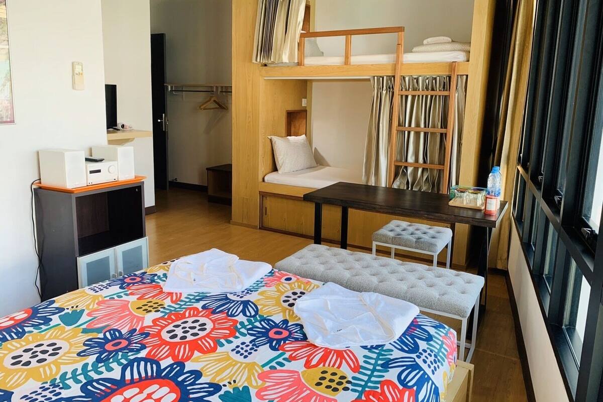 A room with a bunk bed, a small table, a bench, and a colorful bedspread.