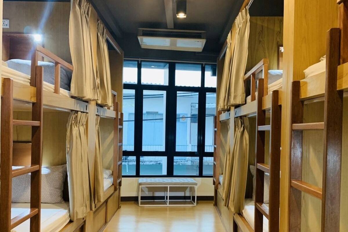A corridor with bunk beds, wooden walls, a bench, and large windows.