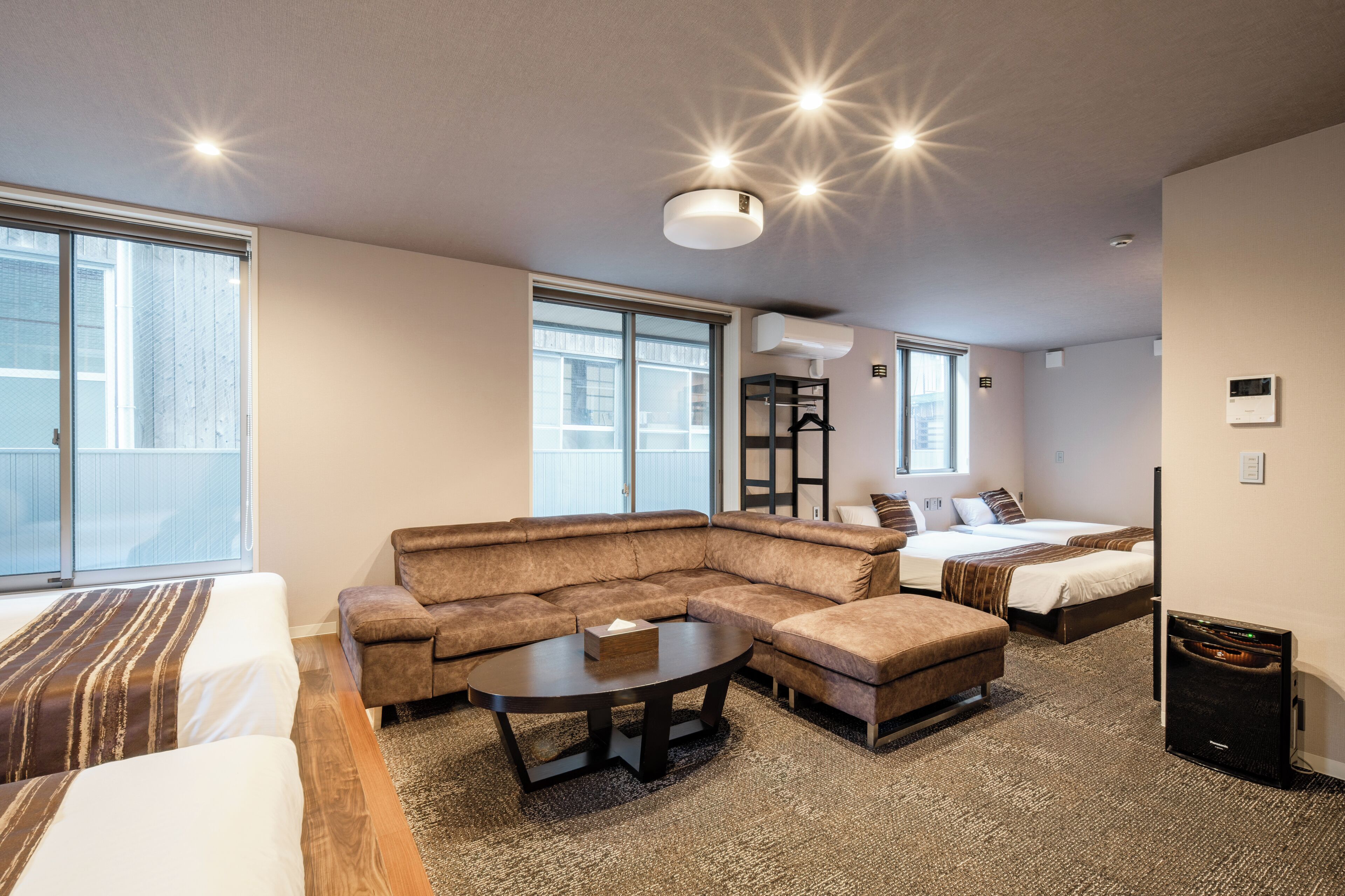 A modern hotel room with a sectional sofa, a round coffee table, a bed, and a small table with a lamp.